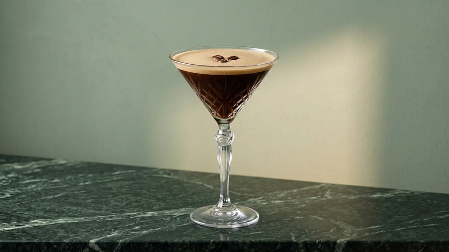 Espresso Martini mit feiner Schaumkrone und drei Kaffeebohnen in einem Kristall-Martiniglas auf grünem Marmor