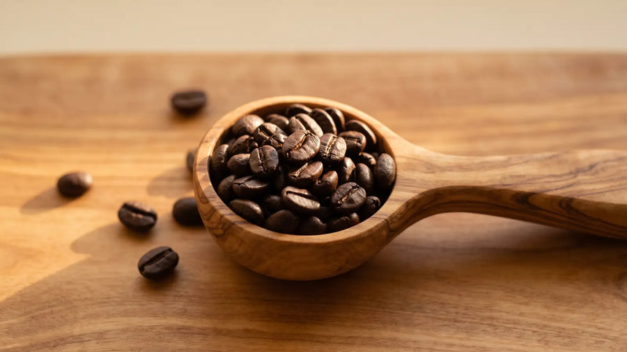 Dunkel geröstete Espressobohnen in einem Messlöffel aus Olivenholz, daneben einzelne Bohnen