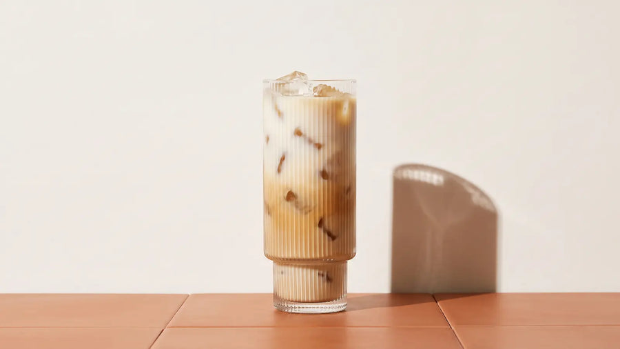 Iced Coffee Latte mit Eiswürfeln und Milch-Kaffee-Verlauf in einem hohen Rillenglas in der Mittagssonne