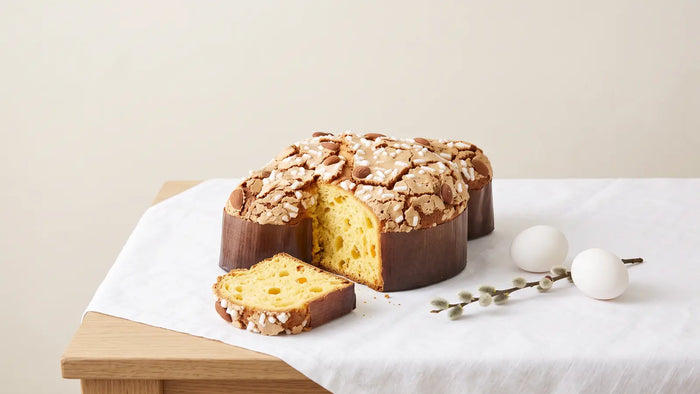 Angeschnittene Colomba Pasquale mit Mandelglasur, Hagelzucker und Mandeln auf weißem Leinen, daneben naturweiße Eier und Weidenkätzchen