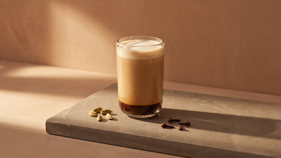 Dirty Chai Latte im Glas auf Stein, daneben Kardamom und Nelken