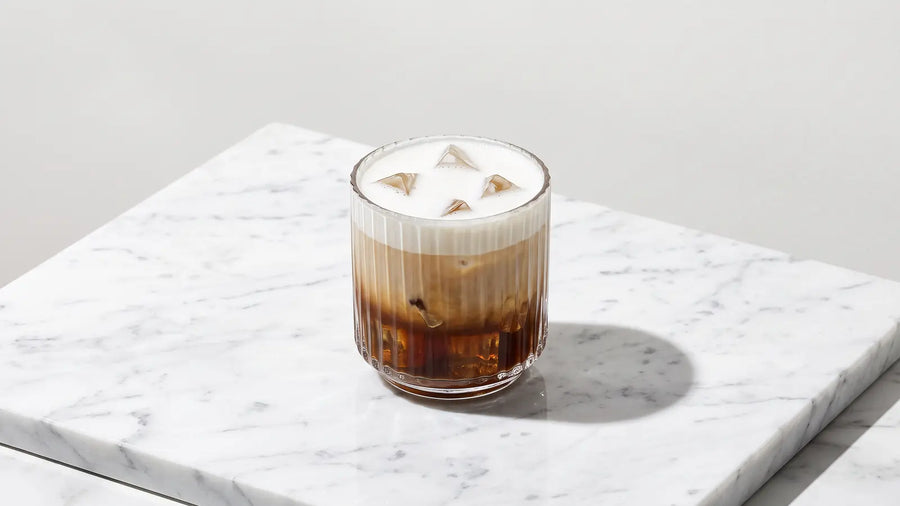 Iced Cappuccino im Tumbler: Espresso auf Eis, darüber kalter Milchschaum, auf weißem Marmor