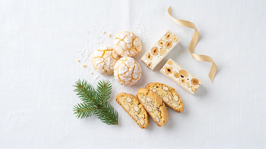 Italienische Süßigkeiten auf weißem Leinen: Amaretti, Torrone mit Nüssen und Cantucci, dazu ein Tannenzweig