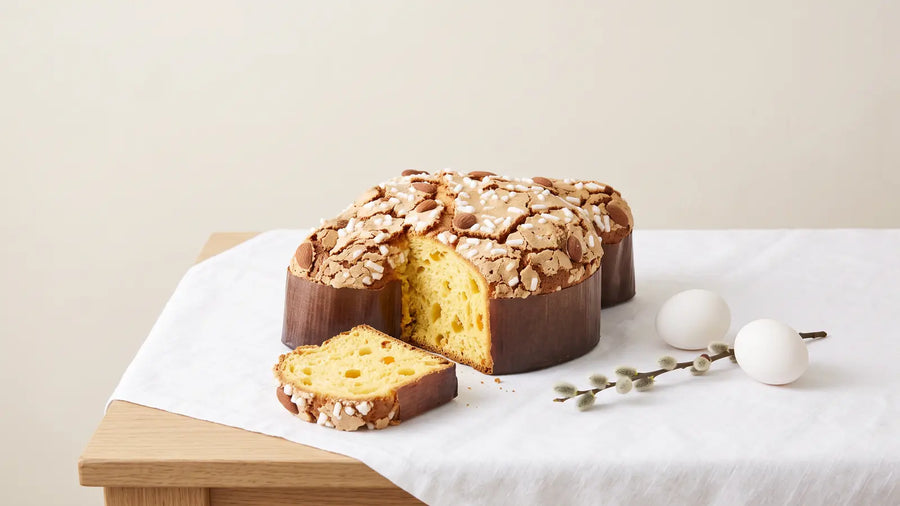 Angeschnittene Colomba Pasquale mit Mandelglasur, Hagelzucker und Mandeln auf weißem Leinen, daneben naturweiße Eier und Weidenkätzchen