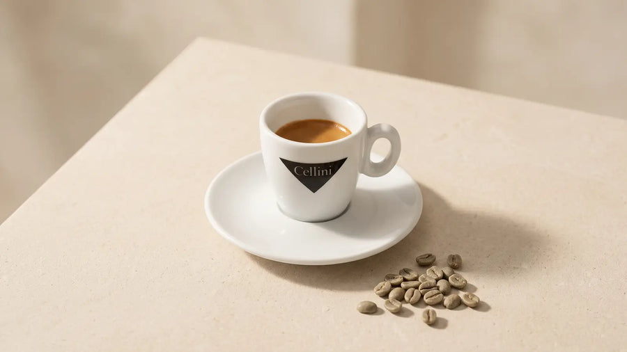 Espresso in der Cellini-Tasse auf hellem Kalkstein, davor grüne, ungeröstete Kaffeebohnen