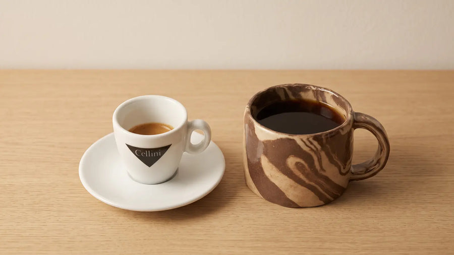Espresso in der Cellini-Tasse neben einem Becher Filterkaffee auf heller Eiche