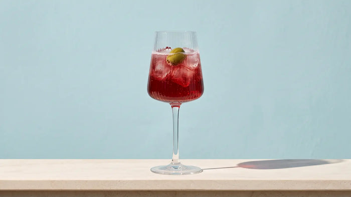 Venezianischer Select Spritz mit Eis und einer grünen Olive in einem Weinglas mit Rillen auf einer hellen Steinbalustrade