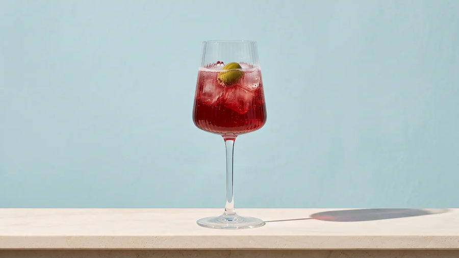 Venezianischer Select Spritz mit Eis und einer grünen Olive in einem Weinglas mit Rillen auf einer hellen Steinbalustrade