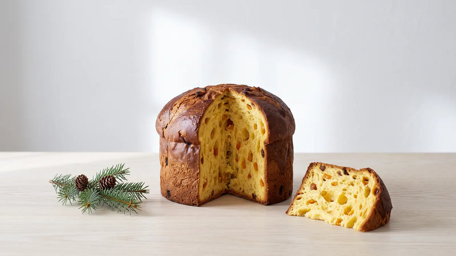 Angeschnittener Panettone mit luftiger Krume, kandierten Orangen und Rosinen, daneben ein Stück und ein Tannenzweig