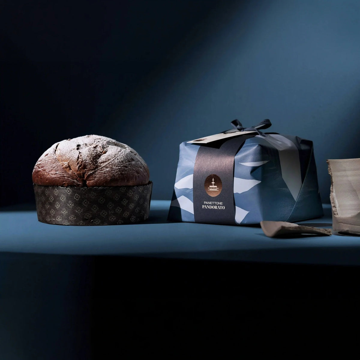 Fiasconaro Panettone Pandorato – Kuchen neben dem eingepackten Produkt, dunkelblaues Studio-Set